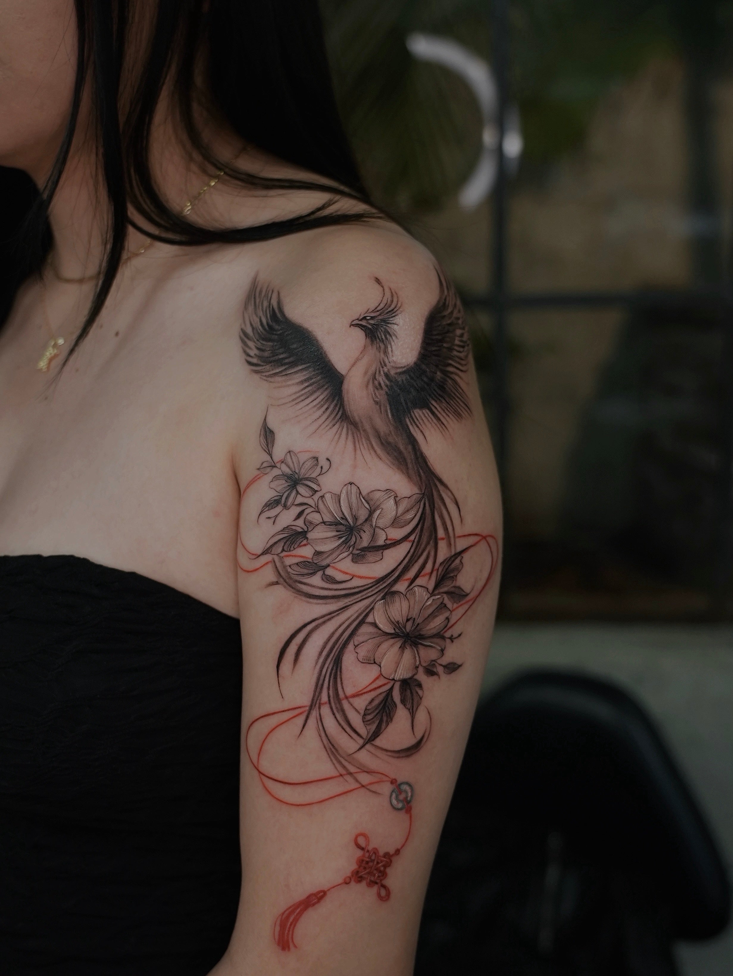 Person with a detailed arm tattoo of a phoenix and flowers, CHINESE STRING STYLE TATTOO. Los Angles California